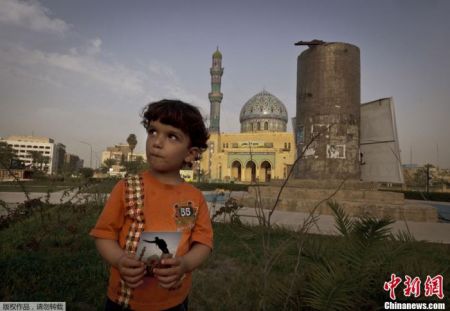 　　资料图：2013年3月14日，伊拉克巴格达，3岁的Hussein站在菲尔杜斯广场上，拿着一张2003年4月9日在同一地点拍摄的美军推倒萨达姆雕像的照片。